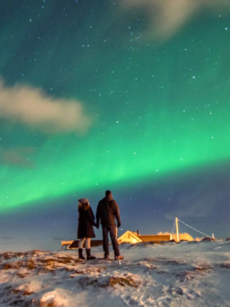 Two people looking at the northern lights in Kirkenes in winter, seen from behind.