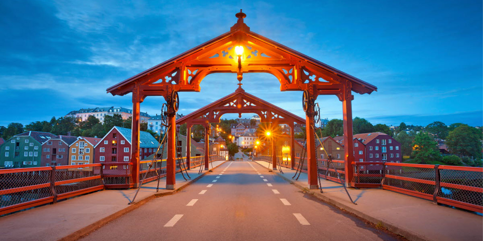 Old Town Bridge in Trondheim. Paved walkway with two red arches at both ends of the bridge. Red handrails on each side. Bakklandet in the background.