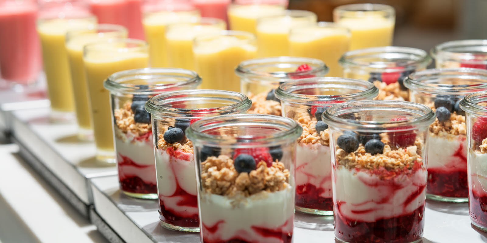 Yoghurt in glass jars, homemade with jam on the bottom, and topped with granola and fresh berries. 