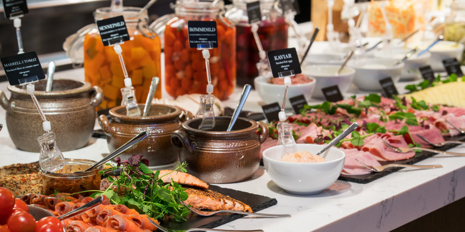 Breakfast is served at Thon Hotel Ski showing a part of the buffet counter, displaying smoked salmon, pepper mackerel, ham and salami.