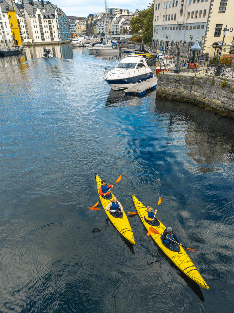 Twee kajakken met 4 personen op weg vanuit het centrum van Ålesund, in Brosundet. Op de achtergrond is het centrum van Ålesund te zien.