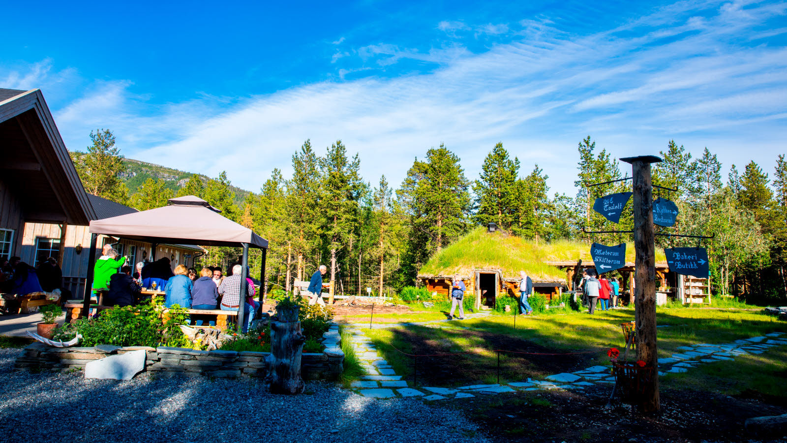 Gæster sidder og spiser på træbænke hos Trasti og Trine.