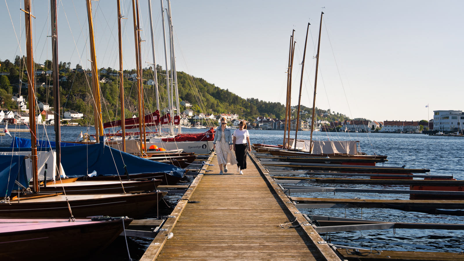 Twee vrouwen wandelen op een pier, omringd door boten.