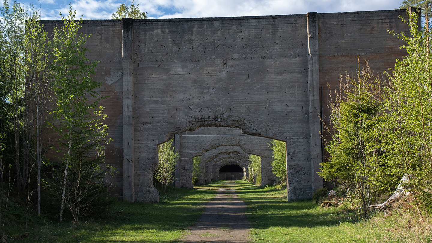 Passasje i murvegger som står på rekke nedover Trandumskogen. Grønn vegetasjon rundt murene. 
