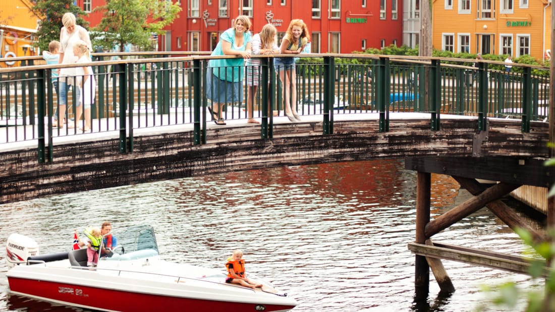 Fiskebryggen i Kristiansand med familie som står på bro og ser ned på båd, der passerer