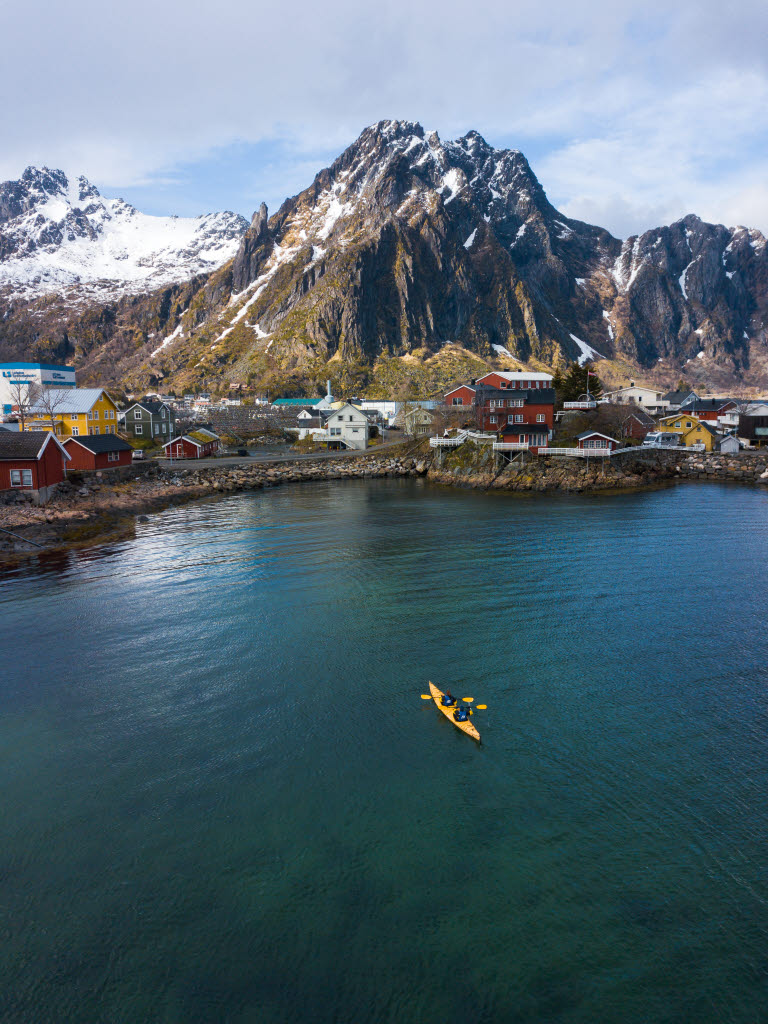 Two RIB boats heading out to sea from the harbour. Thon Hotel Lofoten, Svolvær city centre and snow-covered mountains in the background.