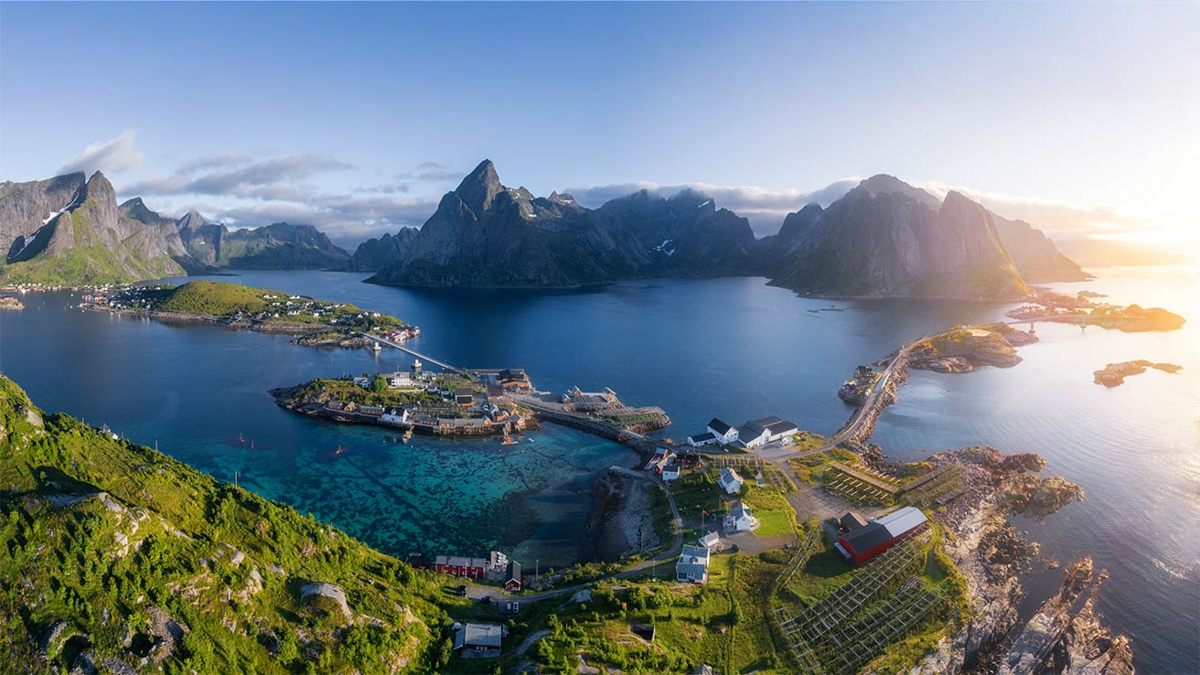 Bergen, blauwe zee en groene natuur bij zonsondergang op de Lofoten, gezien vanaf een bergtop.