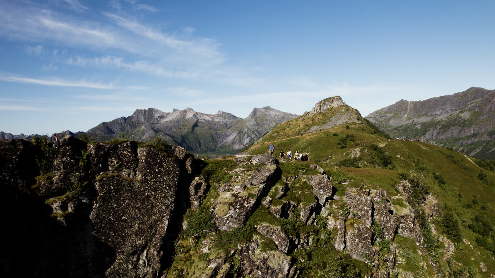 Tour group of seven people hiking in the mountains in sunny weather in Lofoten. Mountains in the background.