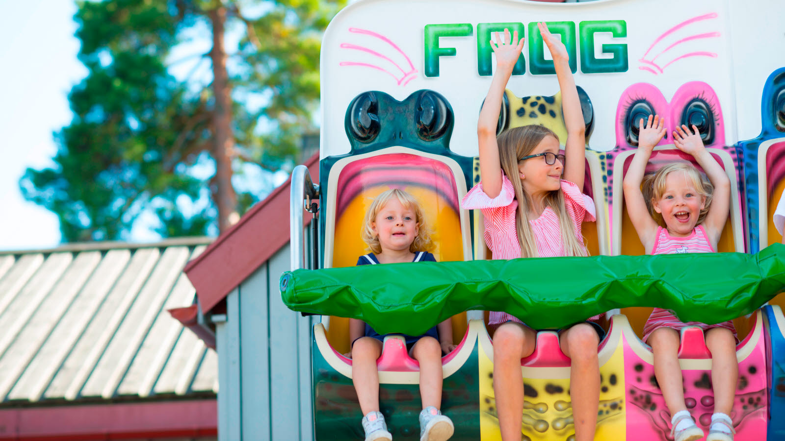 Tre barn sitter i karusellen Frog. Två av barnen har händerna i luften.