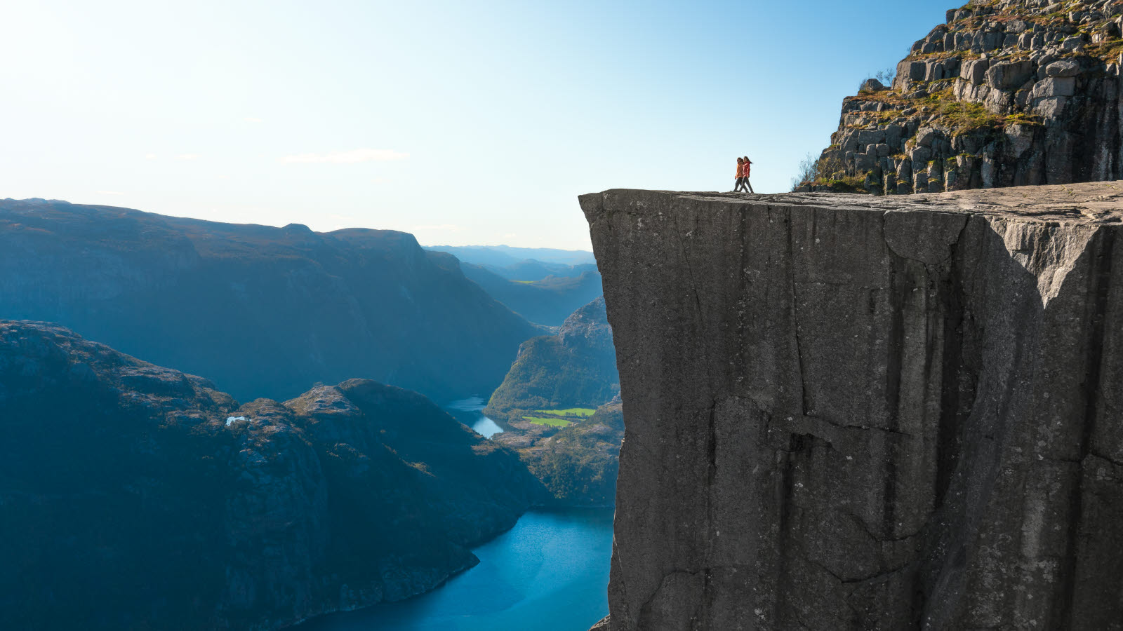 Un homme se tient au bord d’une falaise (Preikestolen) et regarde un lac.