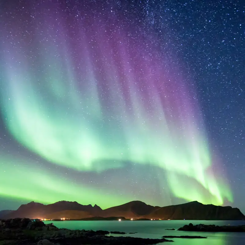 Nordlys i lilla og grønt blafrer over fjord.