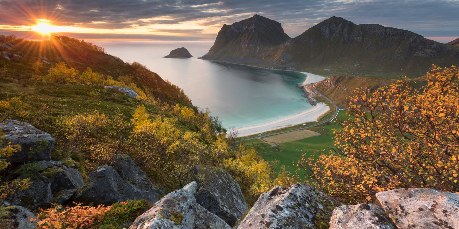 Bilde tatt fra en fjelltopp og ned mot ei strand i solnedgang.