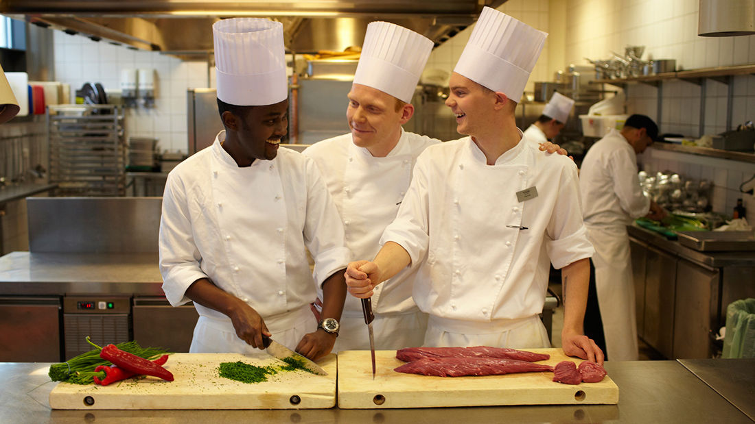 Two trainees receiving guidance from a head chef