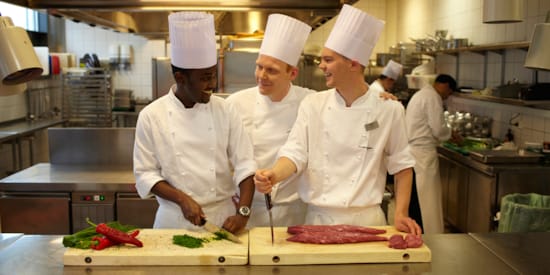 Two trainees receiving guidance from a head chef