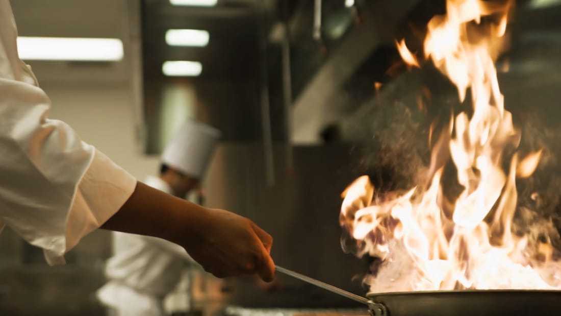 Chef cooks with flames in frying pan at restaurant