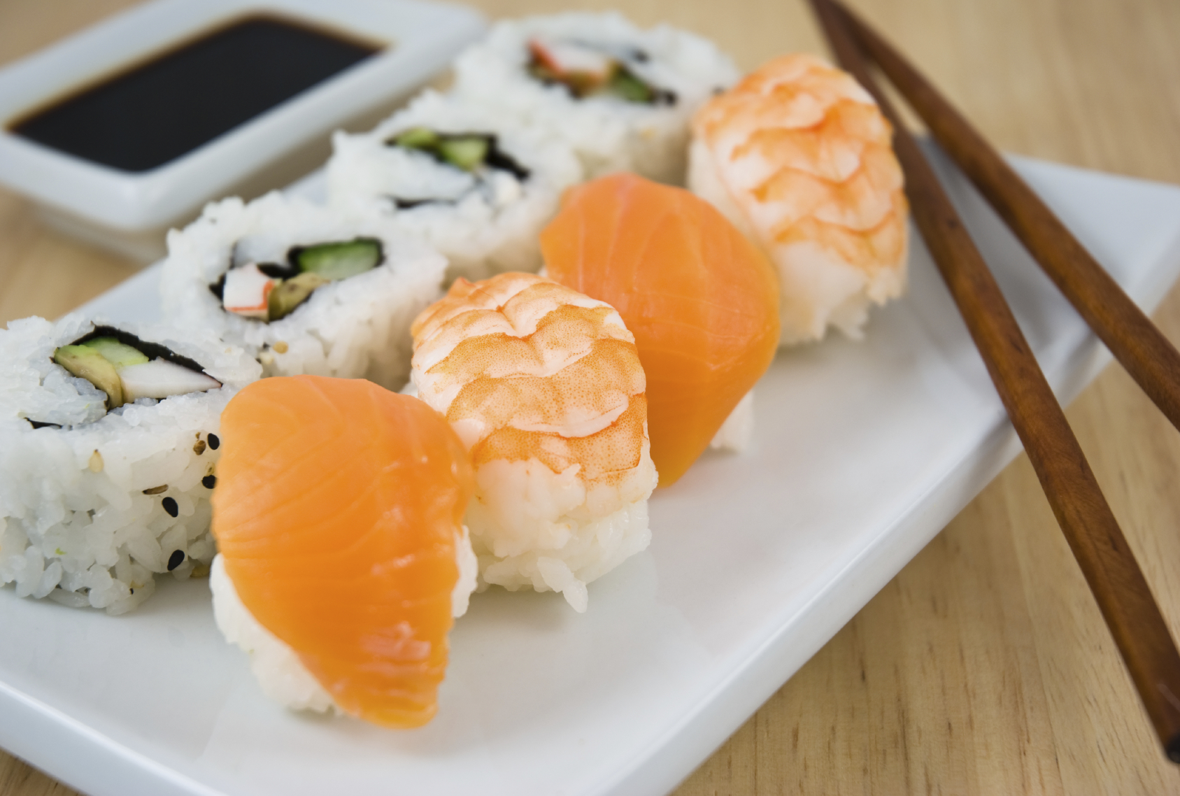 Sushi with salmon and rice, arranged on a white platter on an oak table, with dark wooden chopsticks placed beside the sushi.
