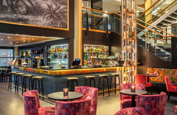 En bar med spennende belysning og røde lenestoler i en hotellobby.