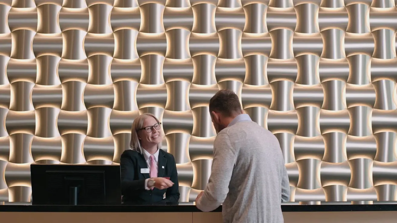 Smilende kvinne som tar i mot mann i resepsjonen på et Thon-Hotell