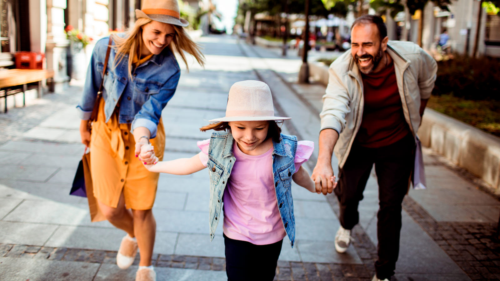 A girl holding her parents by the hand and pulling them after her as she runs down a pedestrian street.