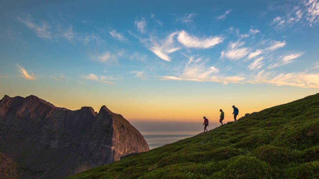 Three people walking down a mountainside at sunset