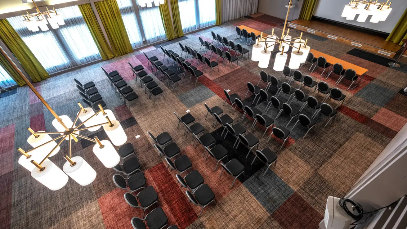 Stor sal med kino oppsett sett ovenfra, lysekroner i taket, store vinduer med gule gardiner, stort lerret foran i lokalet