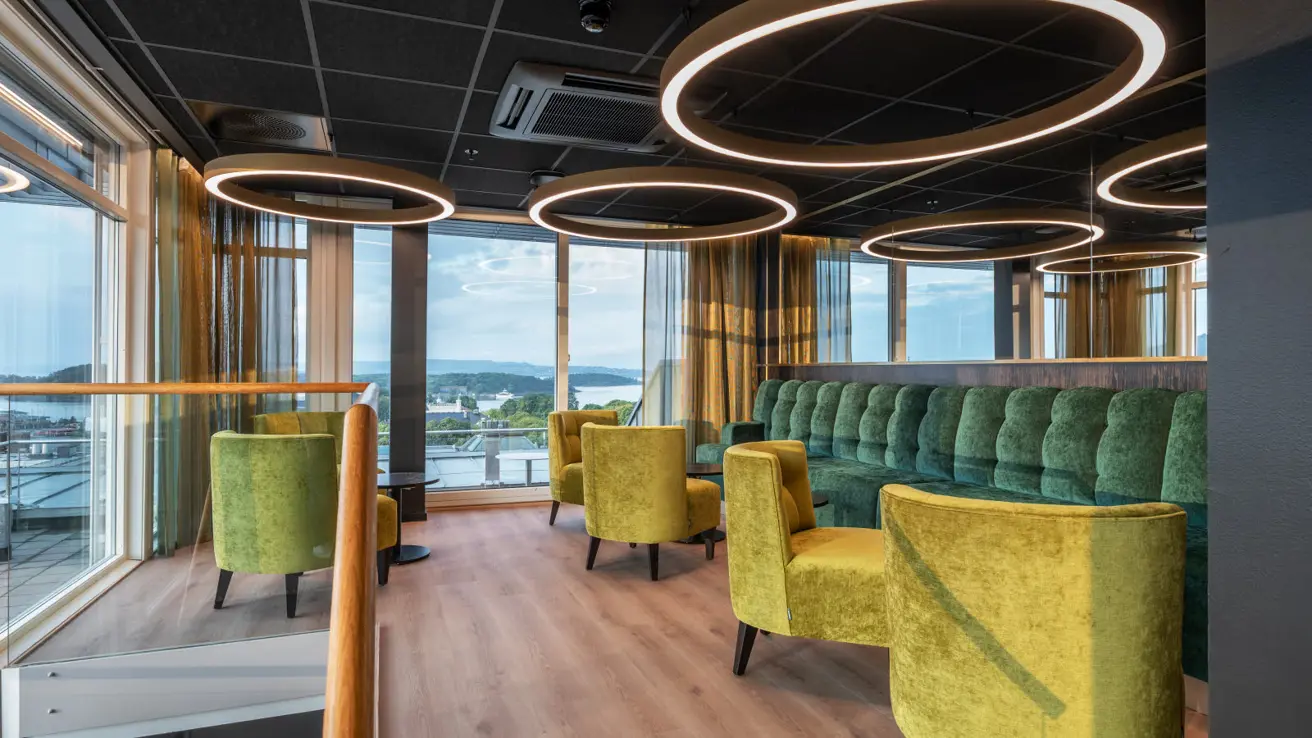 Lounge område tilhørende møterom med flott utsikt og fargerike møbler. Store runde taklamper henger ned og gir en god atmosfære.