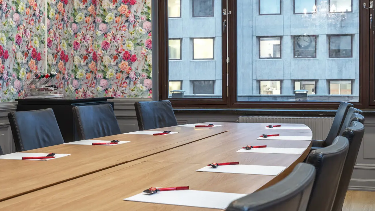 Conference room Stella, 13 seats around an oval table, window, clock and paintings on wall, chandelier hanging from ceiling
